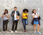 People standing along a wall scrolling social media