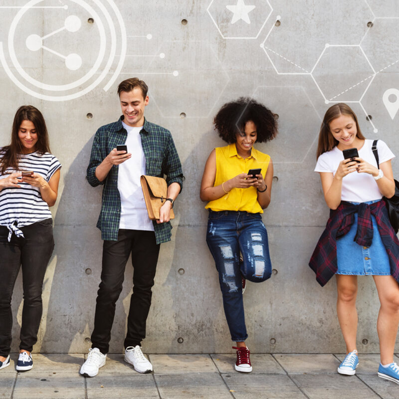 People standing along a wall scrolling social media