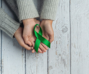 Two hands holding a single green ribbon for mental health